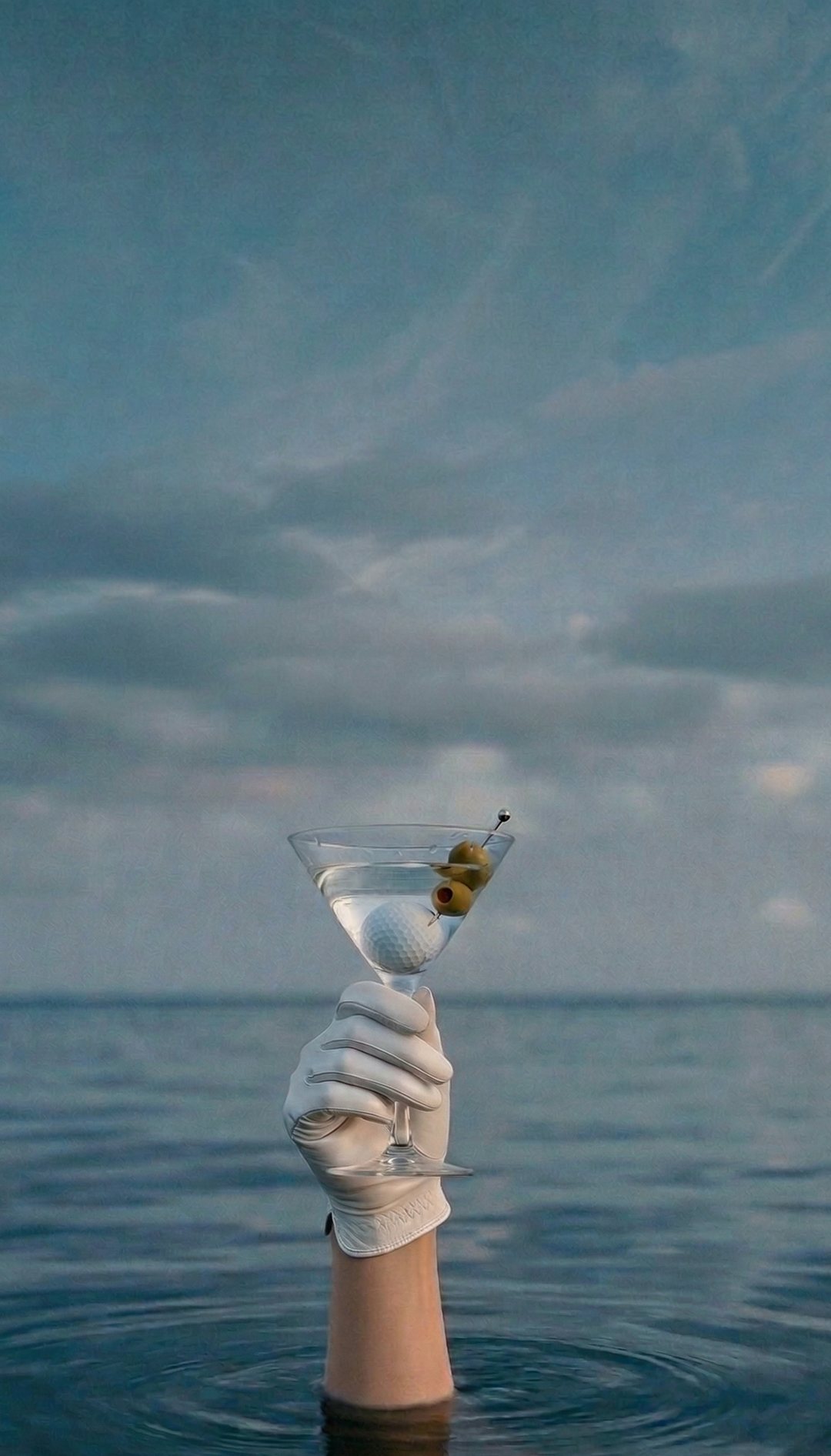 A martini balanced on a golf glove against the ocean
